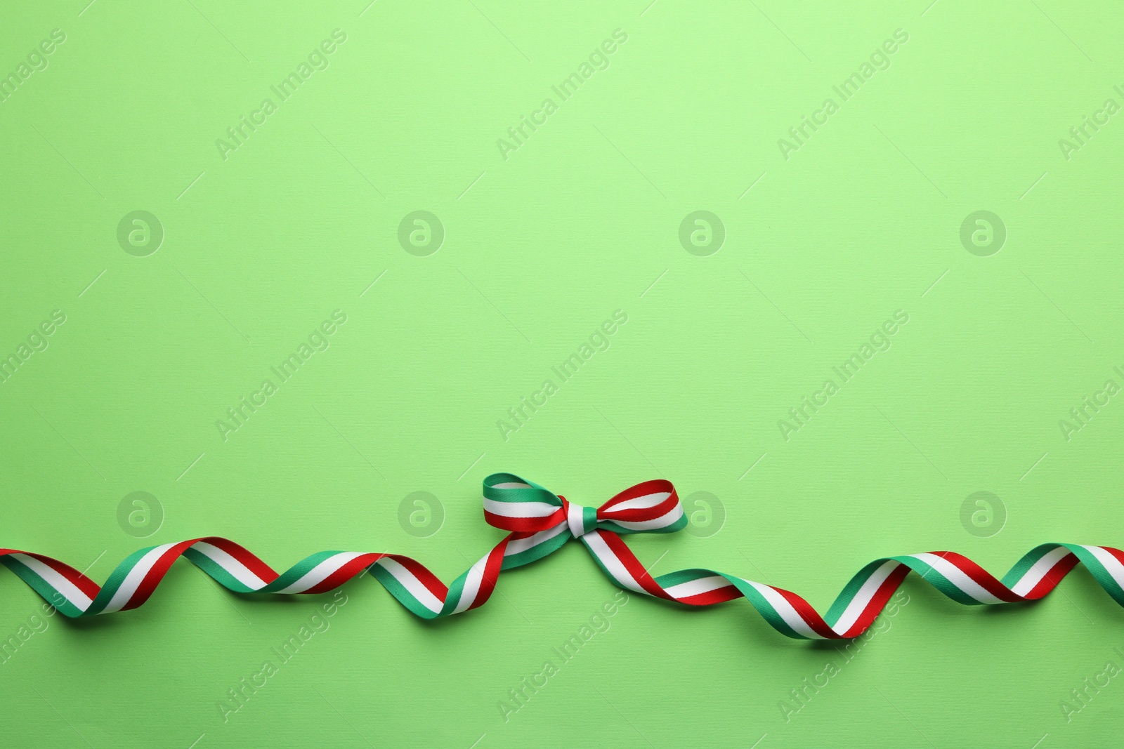 Photo of Ribbon with bow in colors of Hungarian flag on green background, top view. Space for text