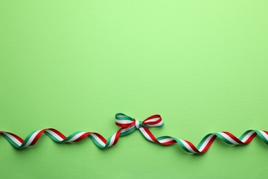 Photo of Ribbon with bow in colors of Hungarian flag on green background, top view. Space for text