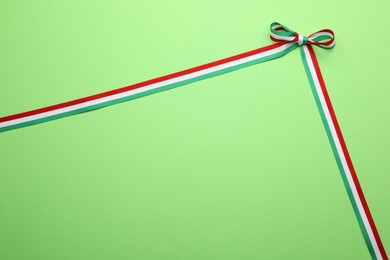 Photo of Ribbon with bow in colors of Hungarian flag on green background, top view. Space for text