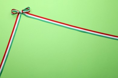 Photo of Ribbon with bow in colors of Hungarian flag on green background, top view. Space for text