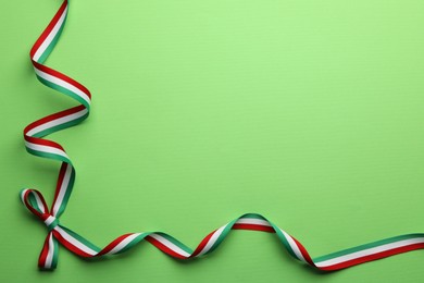 Photo of Ribbon with bow in colors of Hungarian flag on green background, top view. Space for text