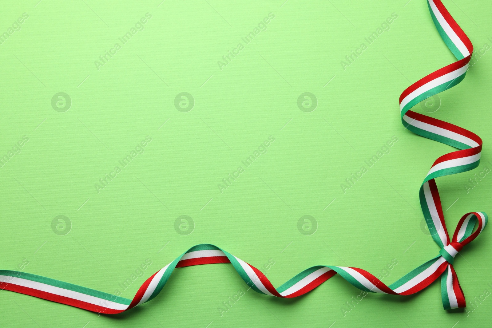 Photo of Ribbon with bow in colors of Hungarian flag on green background, top view. Space for text