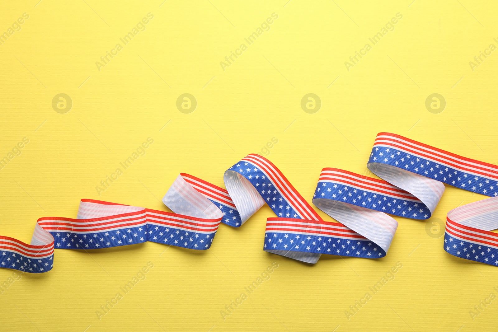 Photo of Ribbon in colors of USA flag on yellow background, top view