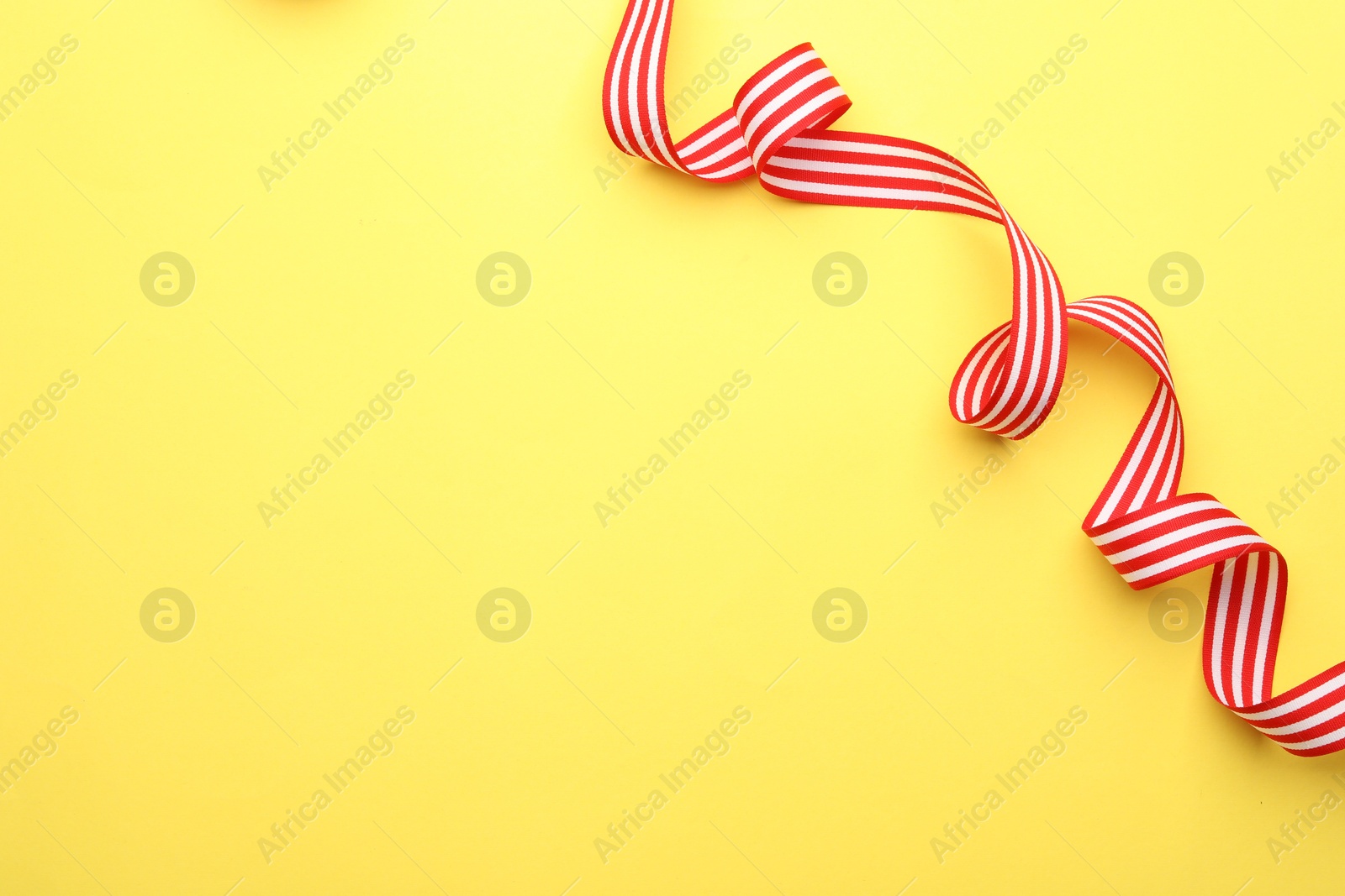 Photo of Striped ribbon on yellow background, top view. Space for text