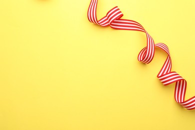 Striped ribbon on yellow background, top view. Space for text