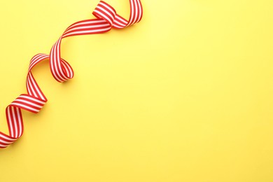 Striped ribbon on yellow background, top view. Space for text