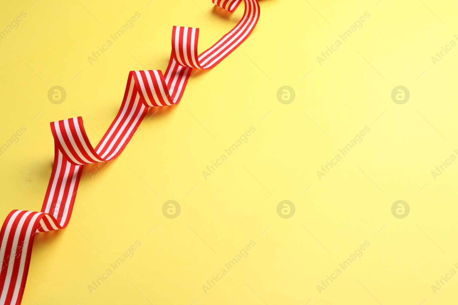 Photo of Striped ribbon on yellow background, top view. Space for text