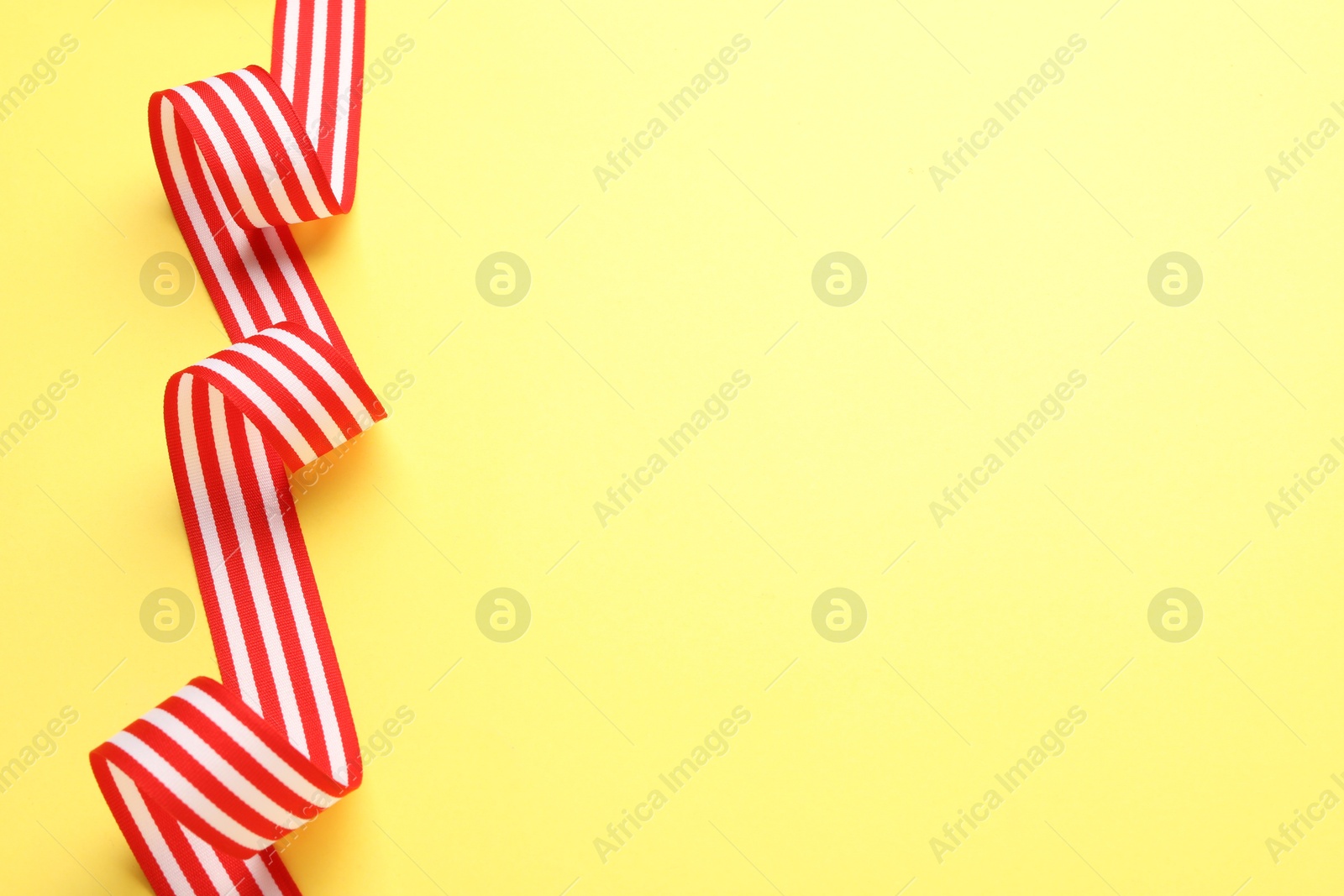 Photo of Striped ribbon on yellow background, top view. Space for text