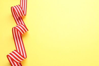 Photo of Striped ribbon on yellow background, top view. Space for text