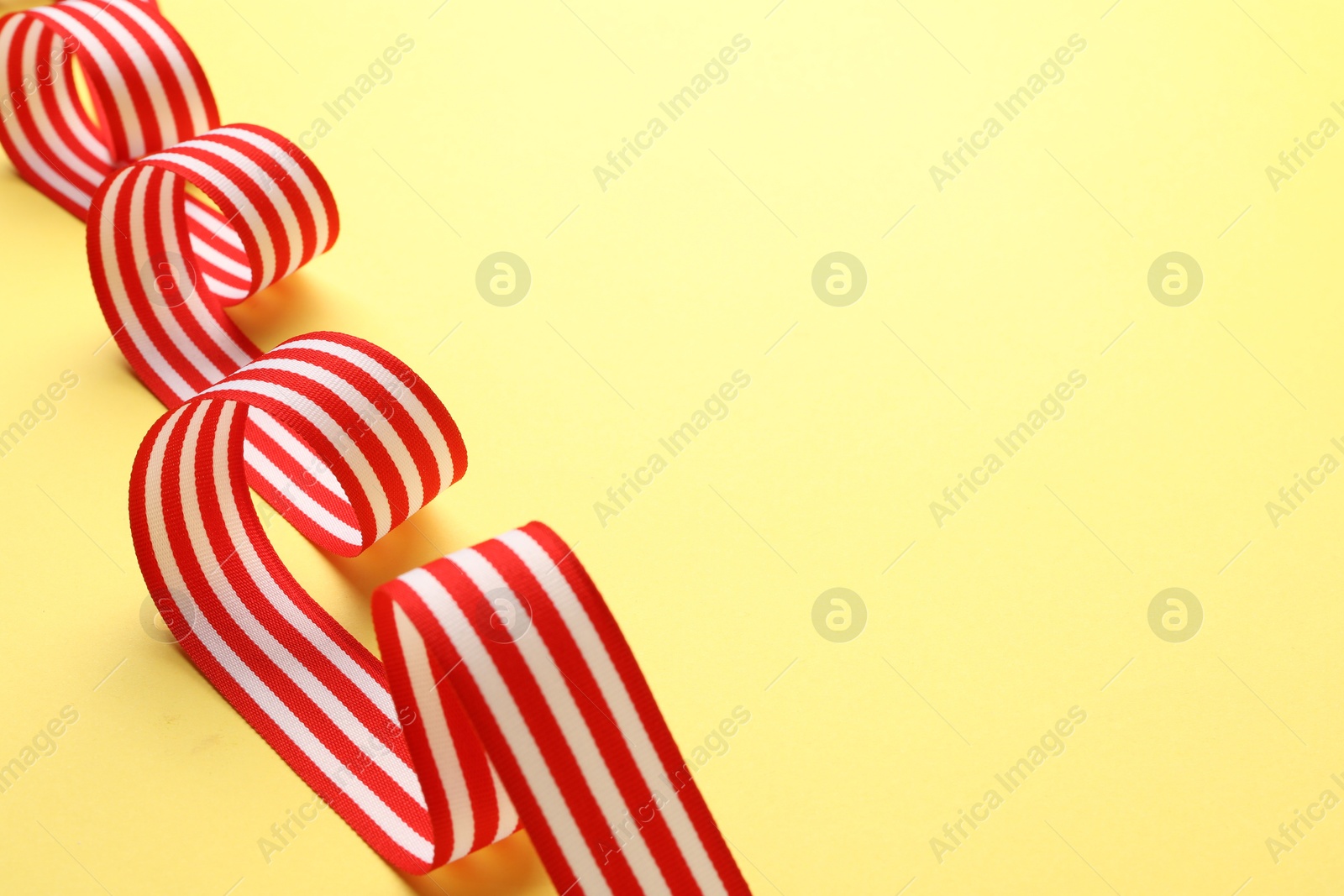 Photo of Striped ribbon on yellow background, closeup. Space for text