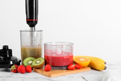 Photo of Hand blender kit, mixtures of ingredients and fresh fruits on white marble table. Space for text