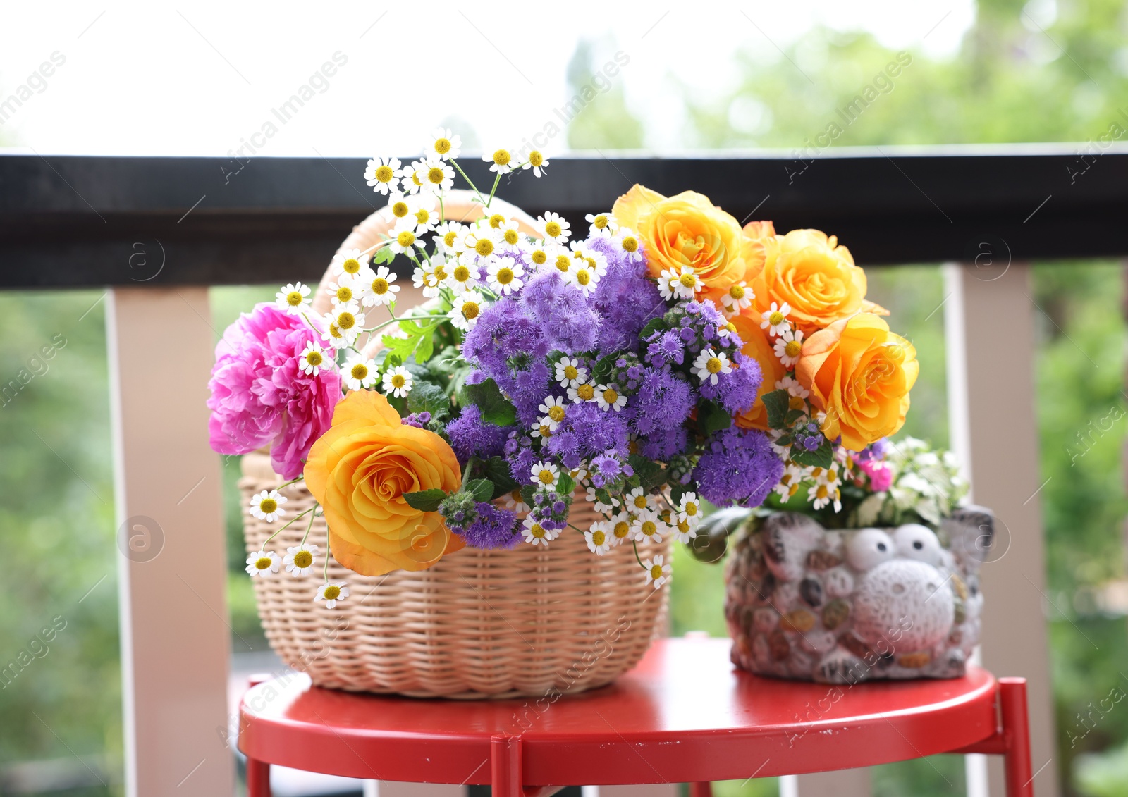 Photo of Wicker basket with beautiful flowers on red table at balcony