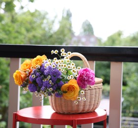 Photo of Wicker basket with beautiful flowers on red table at balcony, space for text