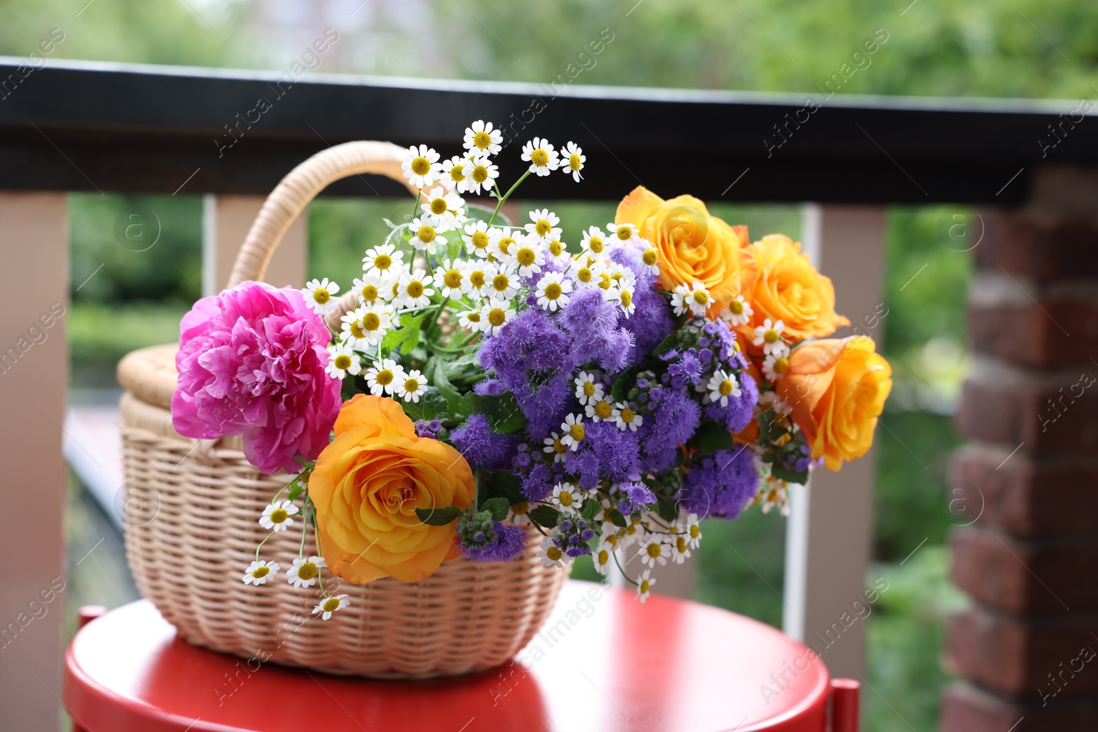 Photo of Wicker basket with beautiful flowers on red table at balcony