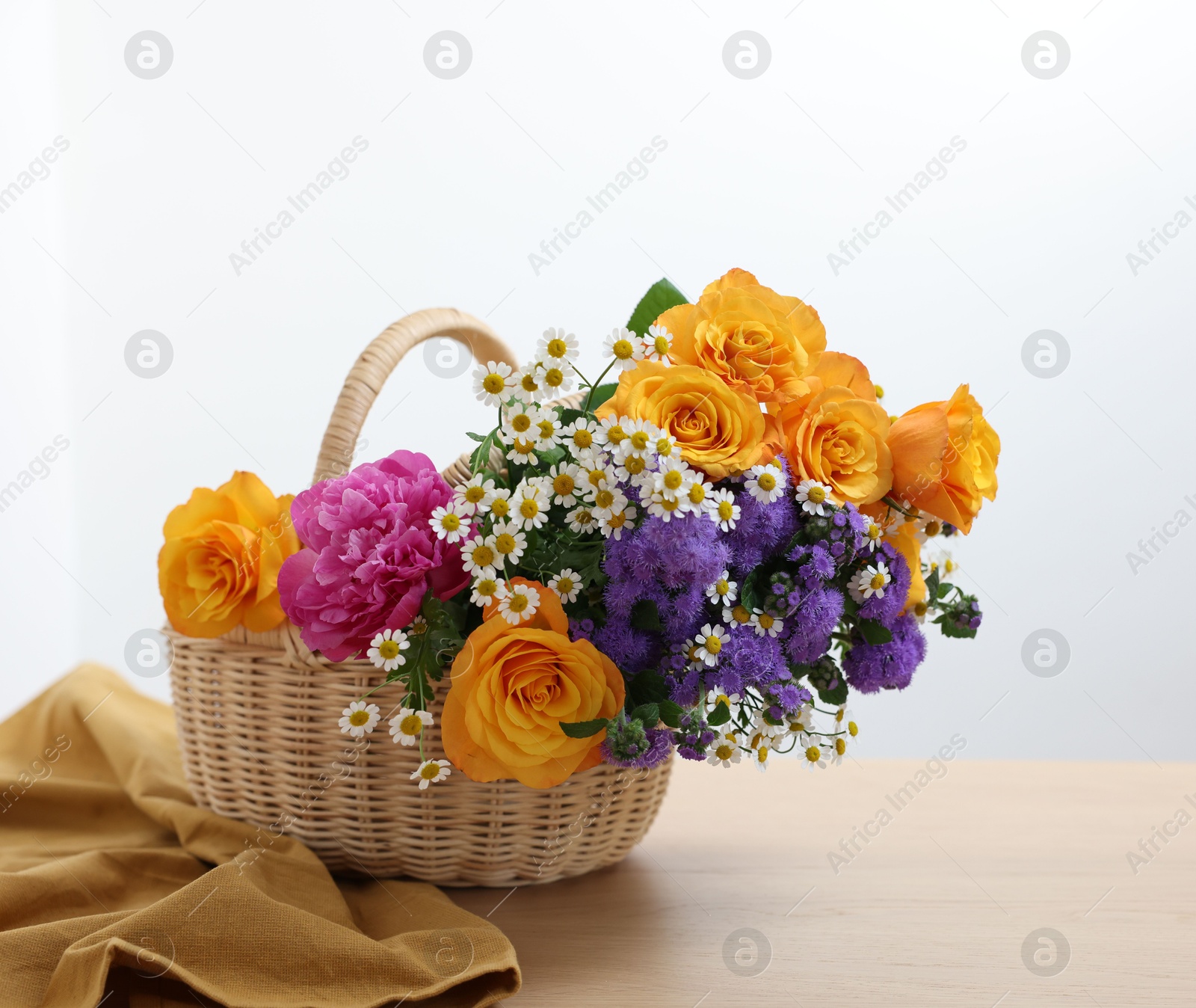 Photo of Wicker basket with beautiful flowers on light wooden table, space for text