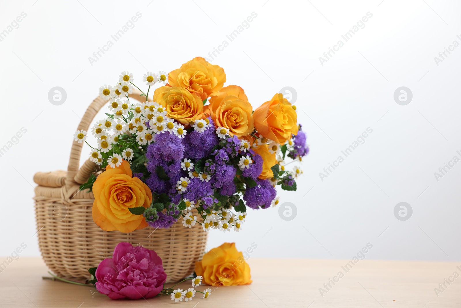 Photo of Wicker basket with beautiful flowers on light wooden table, space for text