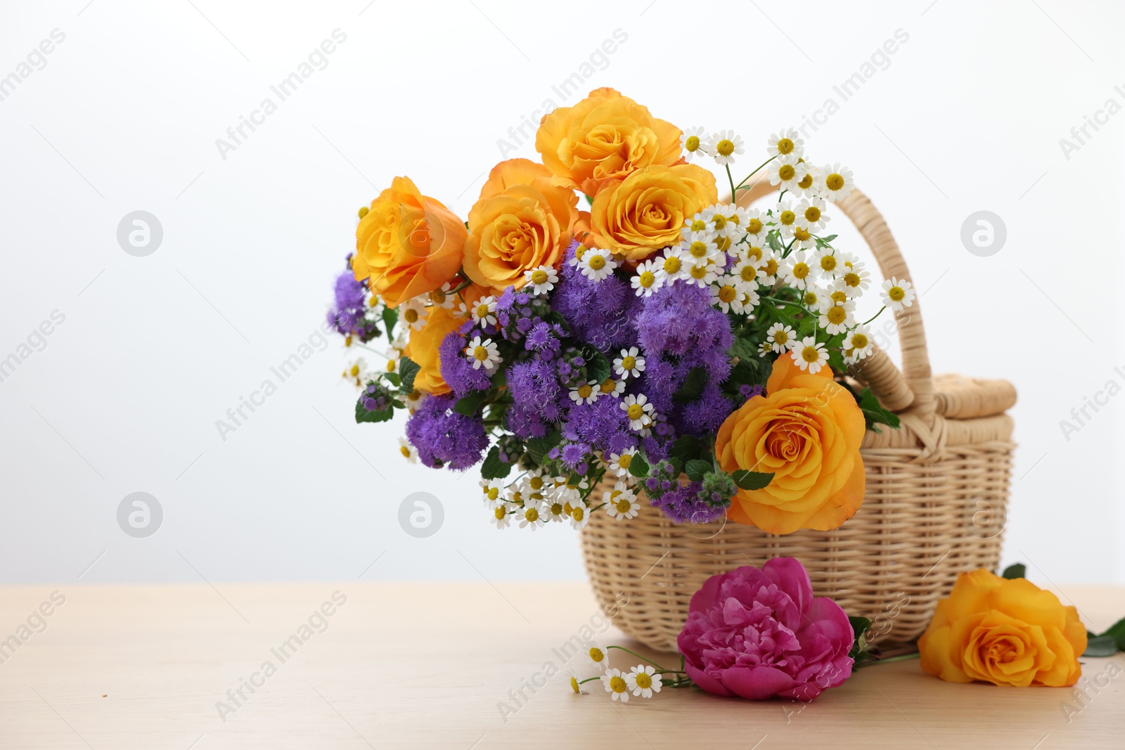 Photo of Wicker basket with beautiful flowers on light wooden table, space for text