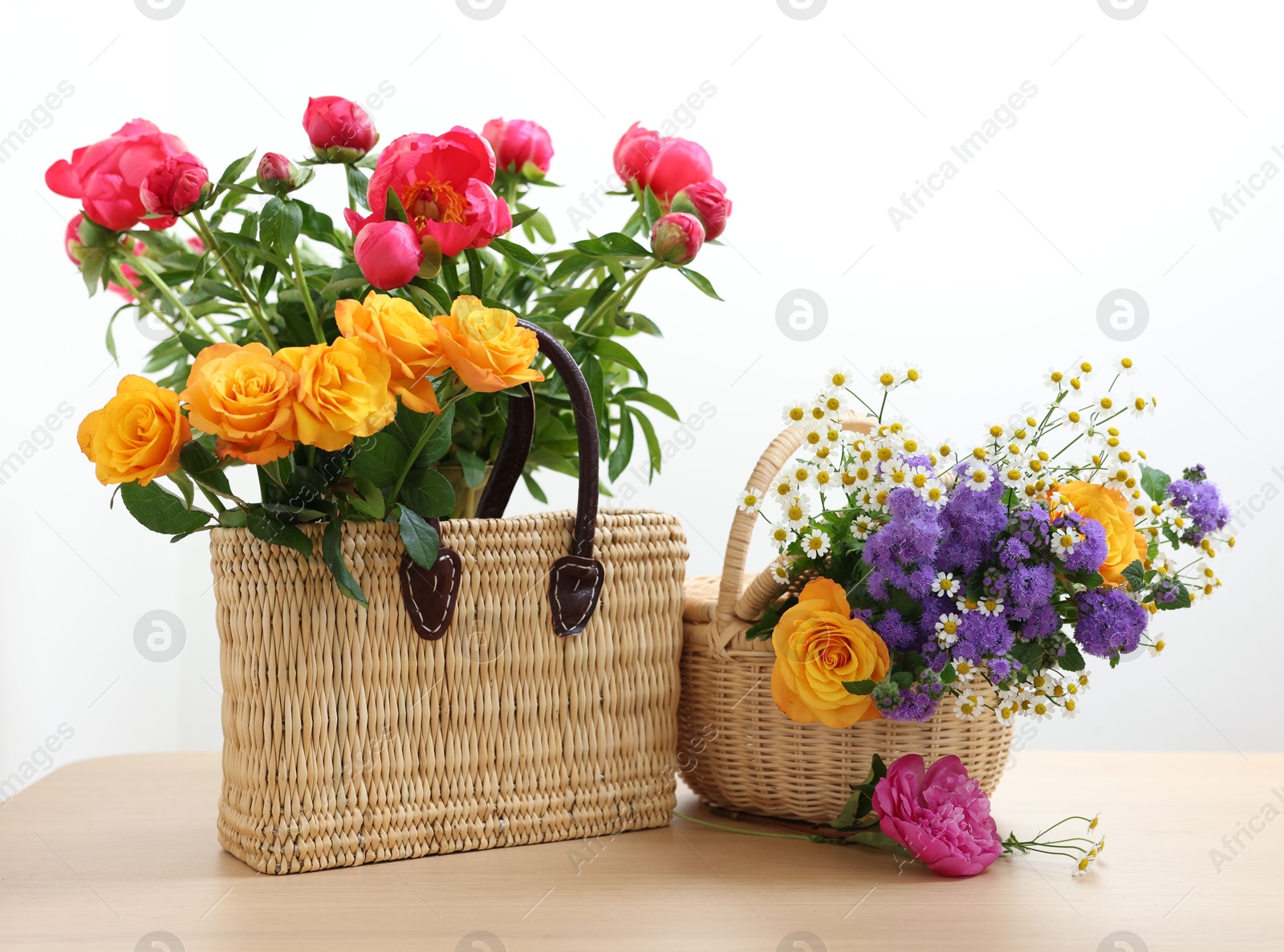 Photo of Wicker baskets with beautiful flowers on light wooden table