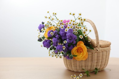 Photo of Wicker basket with beautiful flowers on light wooden table, space for text