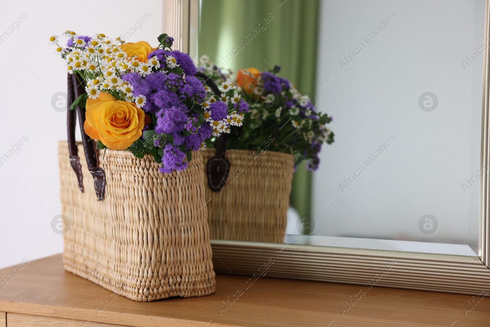 Photo of Wicker basket with beautiful flowers on wooden table indoors, space for text