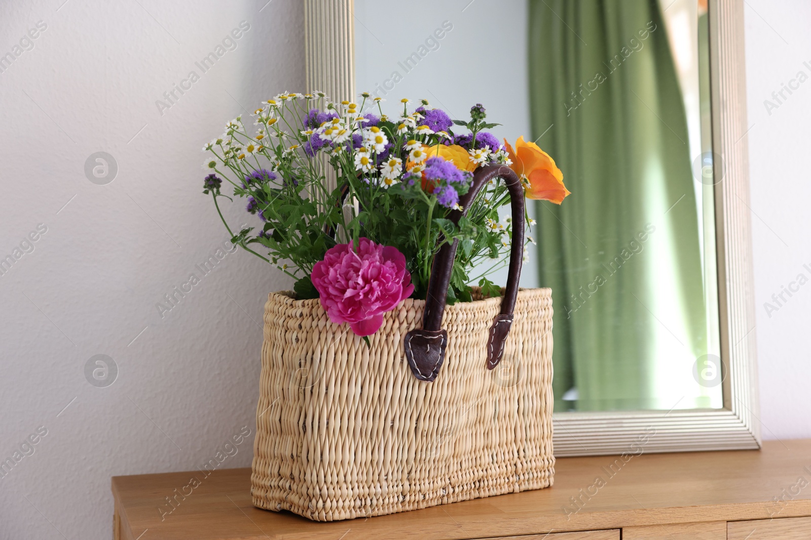 Photo of Wicker basket with beautiful flowers on wooden table indoors