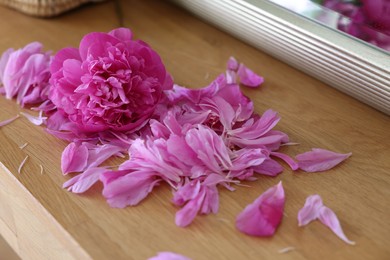 Beautiful pink peony and petals on wooden table indoors, closeup