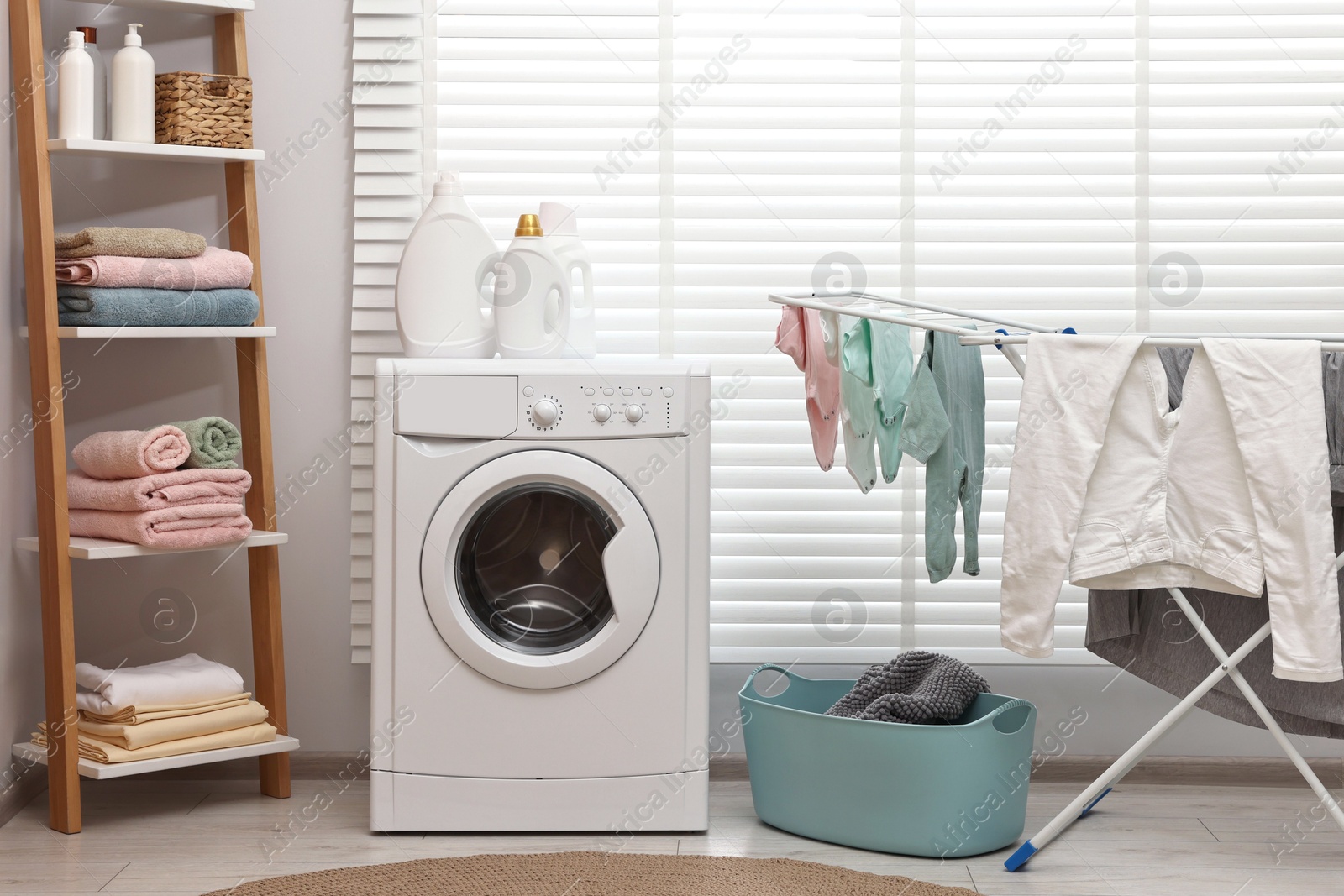 Photo of Washing machine, detergents, towels, basket and drying rack in laundry room