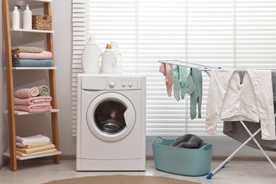 Photo of Washing machine, detergents, towels, basket and drying rack in laundry room