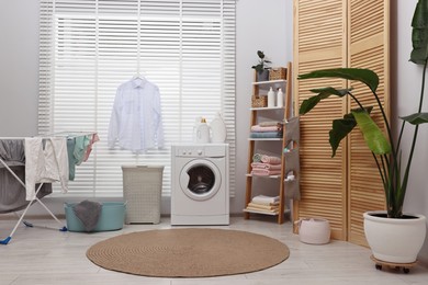 Photo of Washing machine, detergents, towels, baskets and drying rack in laundry room