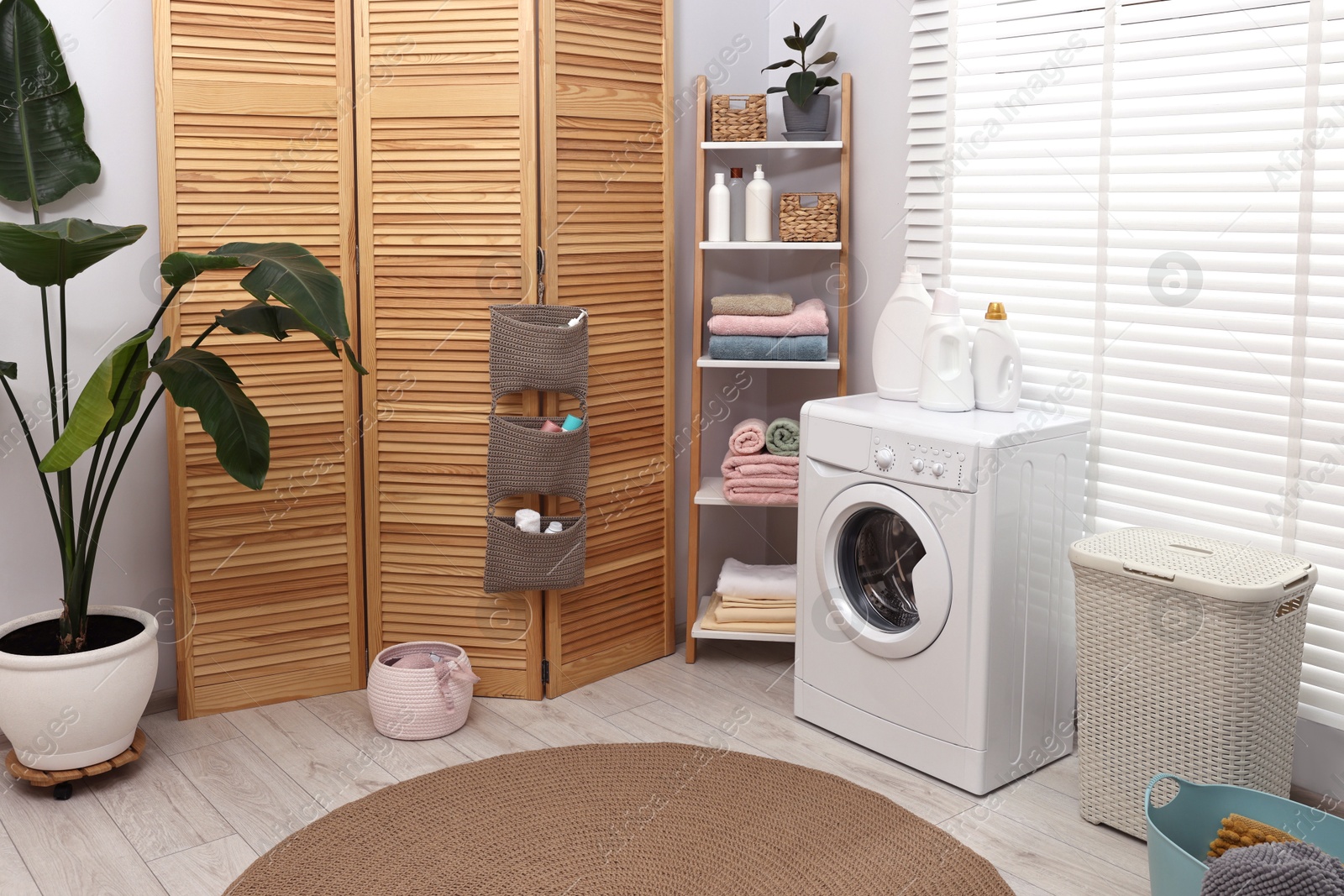 Photo of Washing machine, folding screen, detergents, towels and basket in laundry room