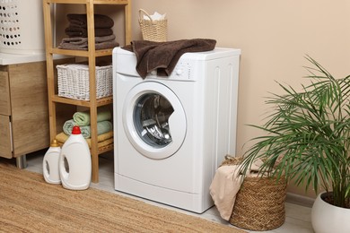 Photo of Stylish laundry room interior with washing machine, furniture, detergents and houseplant