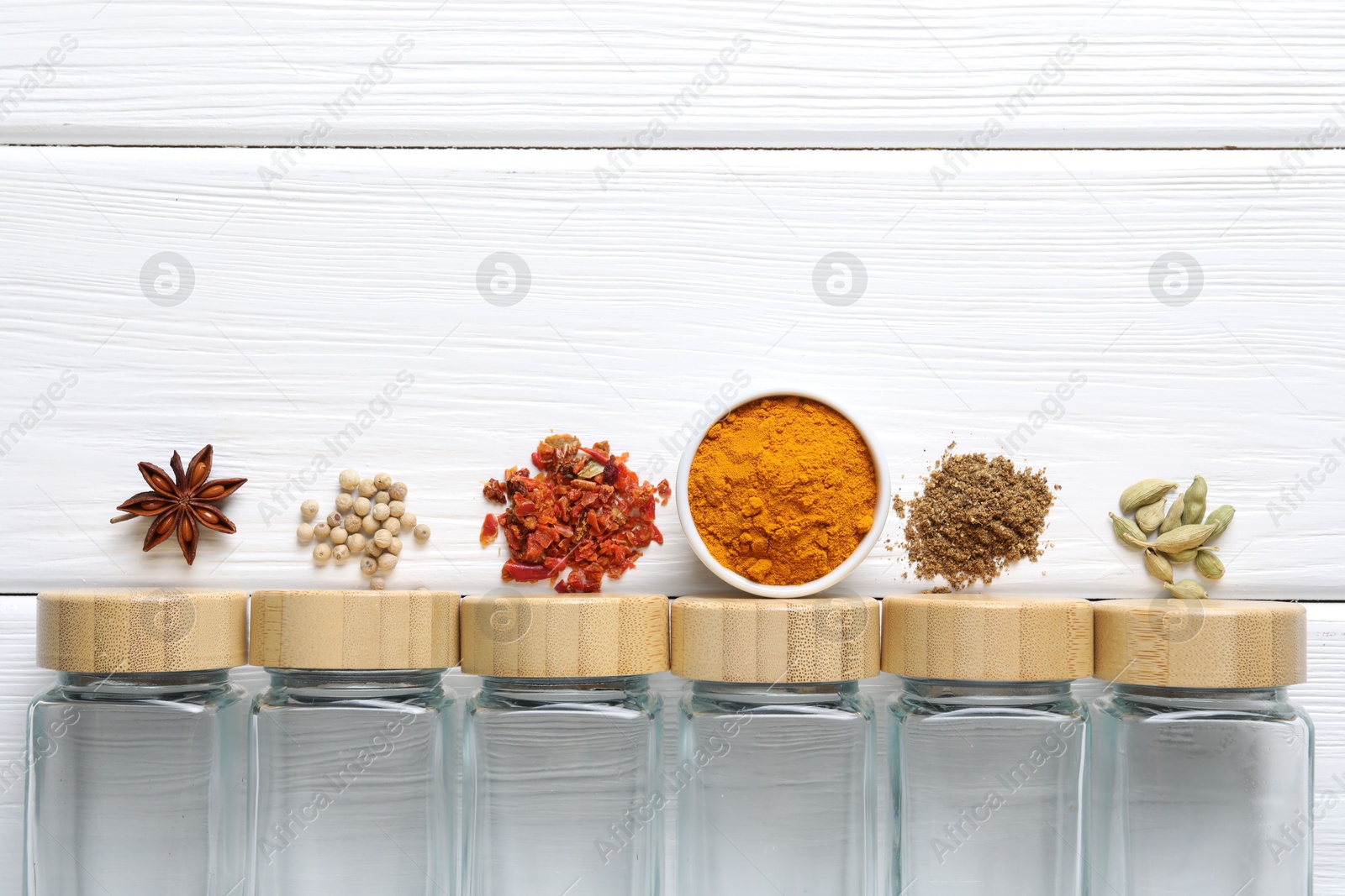 Photo of Different spices and glass jars on white wooden table, top view