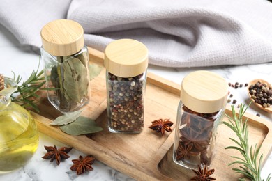 Glass jars with different spices on white marble table