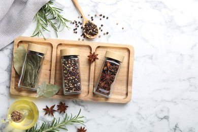 Glass jars with different spices on white marble table, flat lay. Space for text