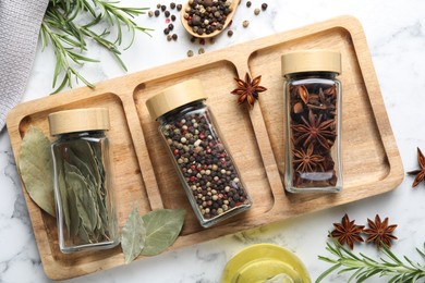 Photo of Glass jars with different spices on white marble table, flat lay