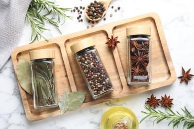 Photo of Glass jars with different spices on white marble table, flat lay