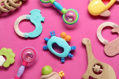 Different baby rattles on pink background, flat lay