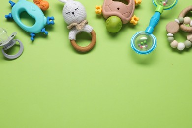 Different baby rattles on green background, flat lay. Space for text