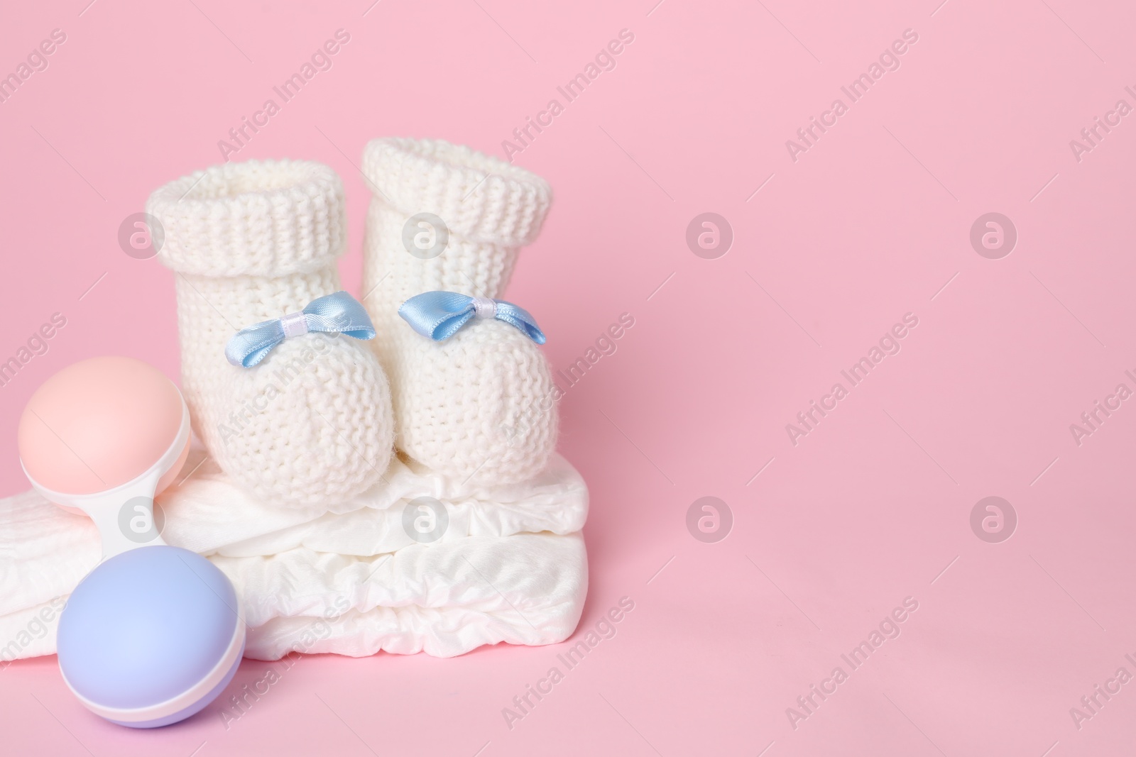 Photo of Baby rattle, booties and diapers on pink background. Space for text