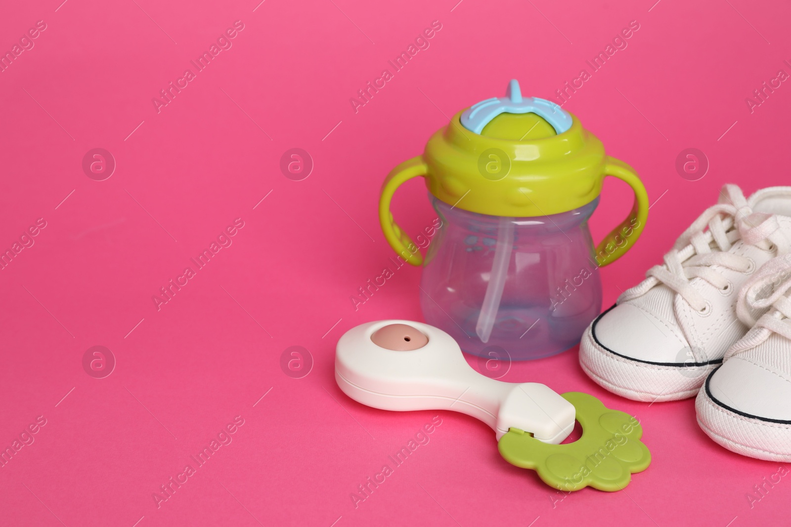 Photo of Baby rattle, bottle and booties on crimson background. Space for text