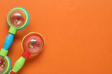 Colorful baby rattles on orange background, flat lay. Space for text