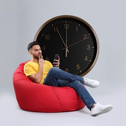 Image of Man with smartphone sitting in beanbag near big clock on grey background