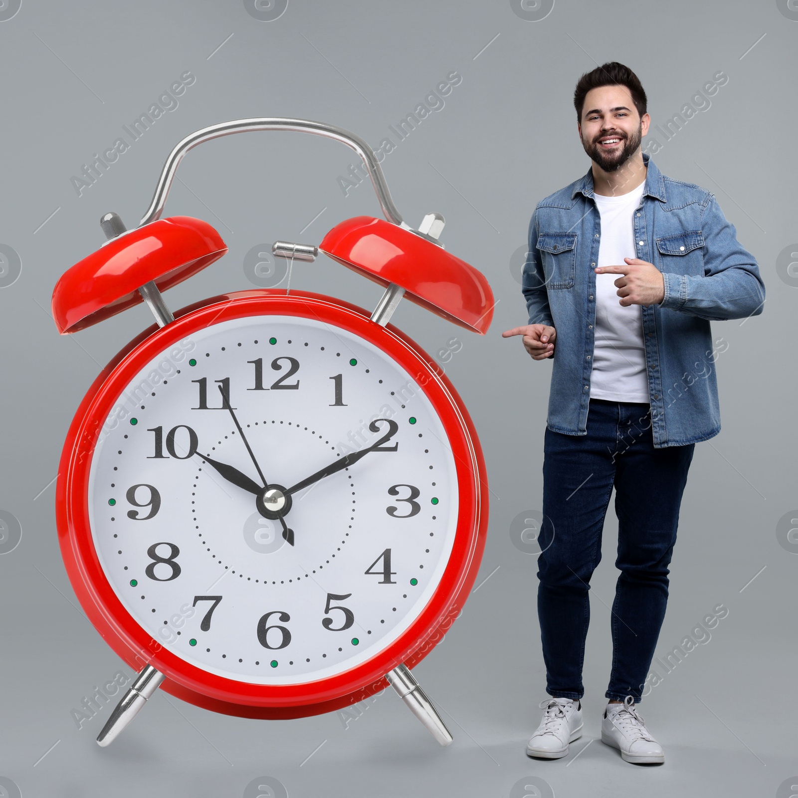 Image of Man pointing at big alarm clock on grey background