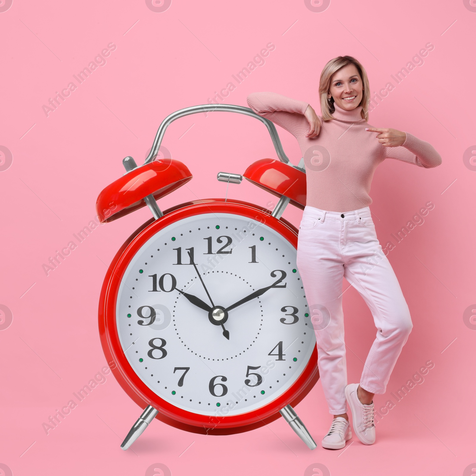 Image of Woman pointing at big alarm clock on pink background