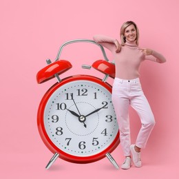 Image of Woman pointing at big alarm clock on pink background