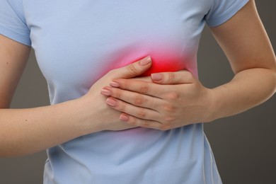 Woman suffering from pain in chest on dark grey background, closeup. Heart disease