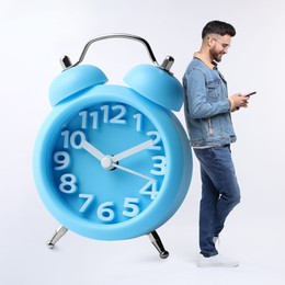 Man with smartphone and big alarm clock on white background