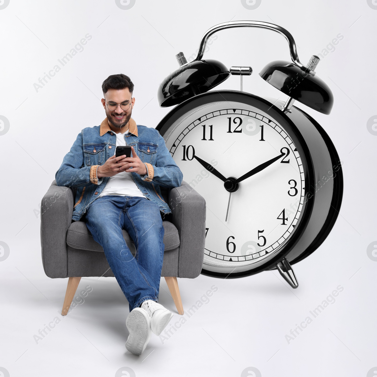 Image of Man with smartphone sitting in armchair near big alarm clock on white background