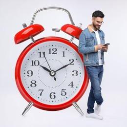 Man with smartphone and big alarm clock on white background