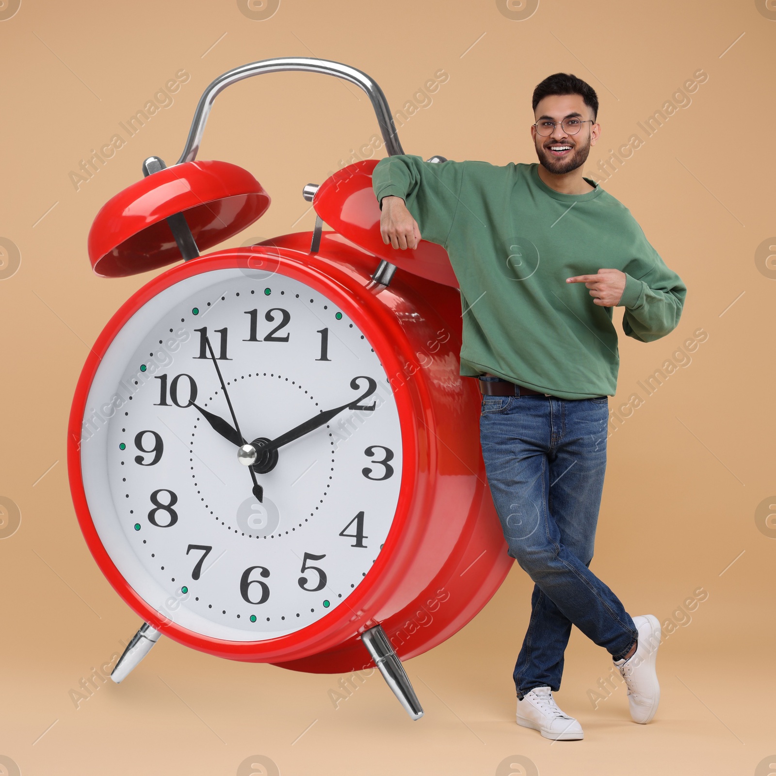 Image of Man pointing at big alarm clock on beige background